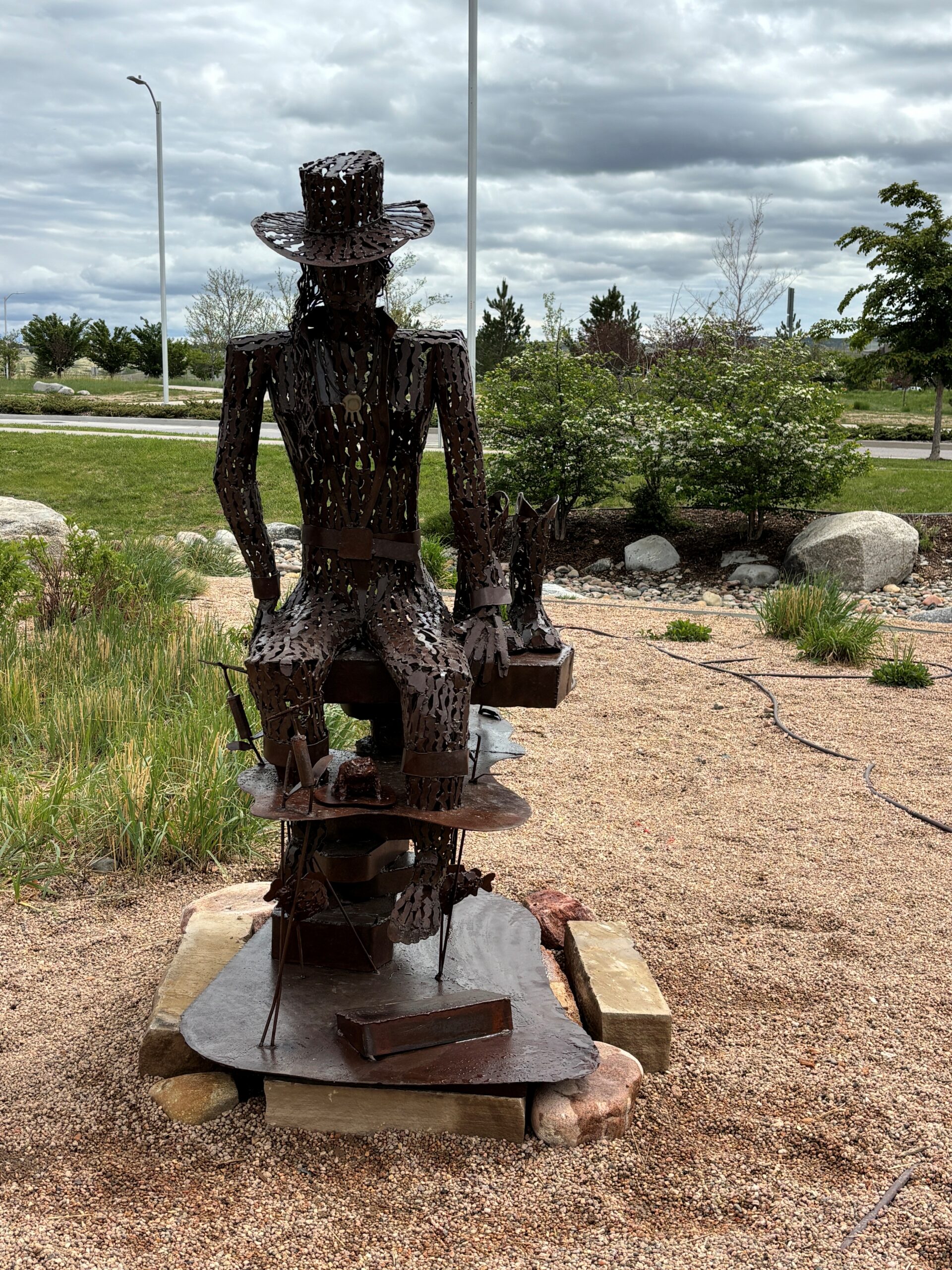 Coolin' Down by Bill Hunting is a coppery-colored, wiry sculpture of a cowboy resting after a hard day of work.