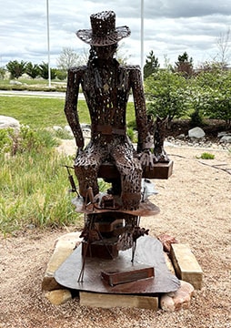 Coolin' Down by Bill Hunting is a coppery-colored, wiry sculpture of a cowboy resting after a hard day of work.