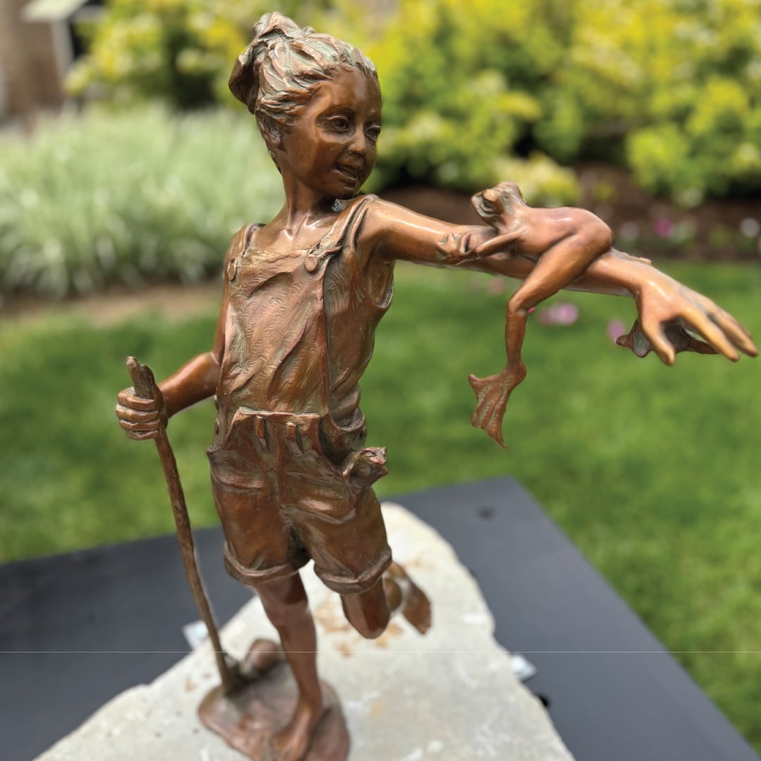 Froggy Summer Day is a bronze sculpture of a little girl with a frog on her arm.