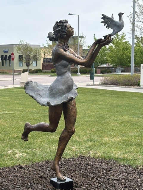 Hope is a bronze sculpture featuring a woman in a dress holding a bird and looking up at it as it flies away.