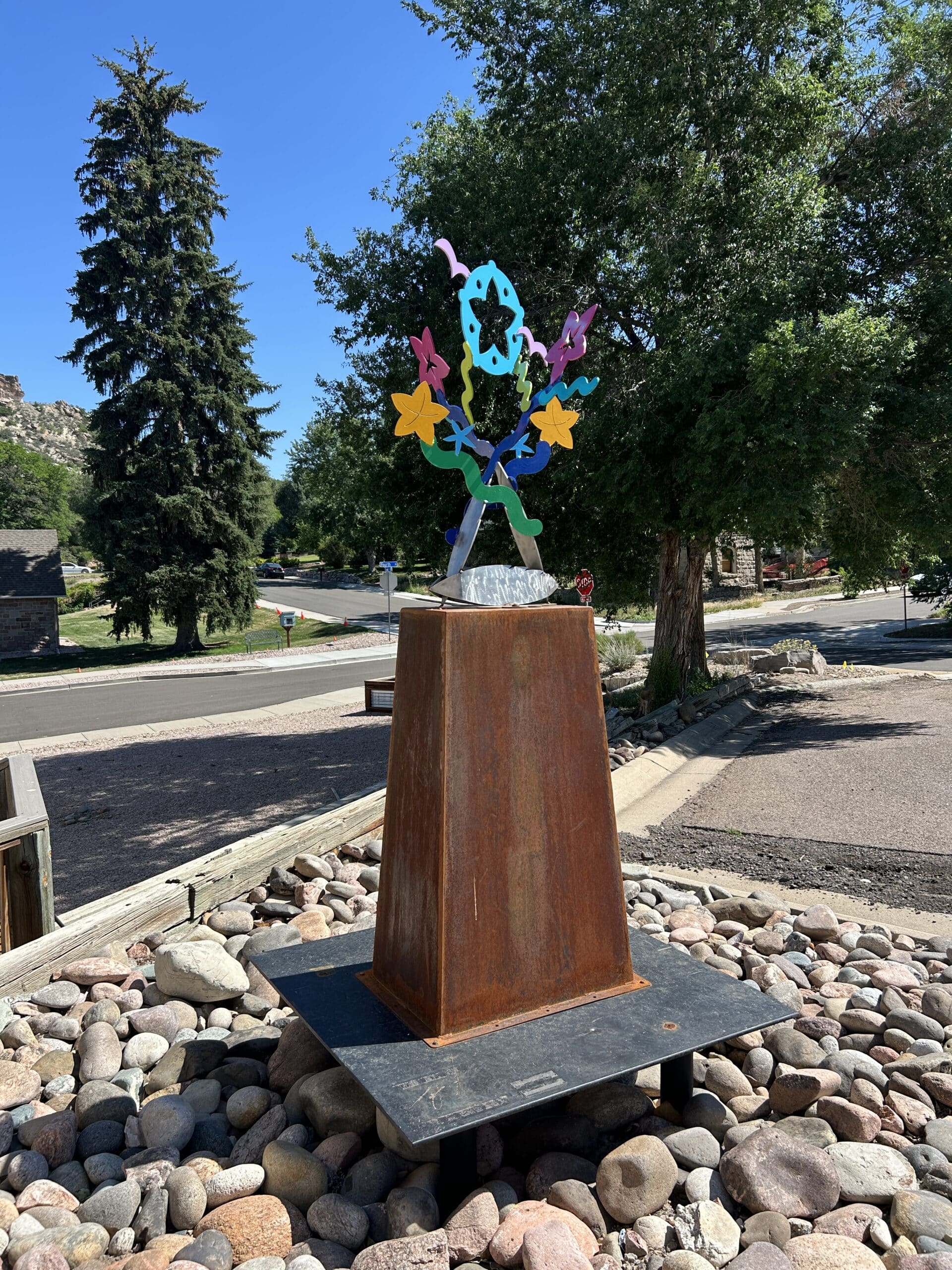 Natural Selection is a colorful metal sculpture that includes natural elements such as flowers.