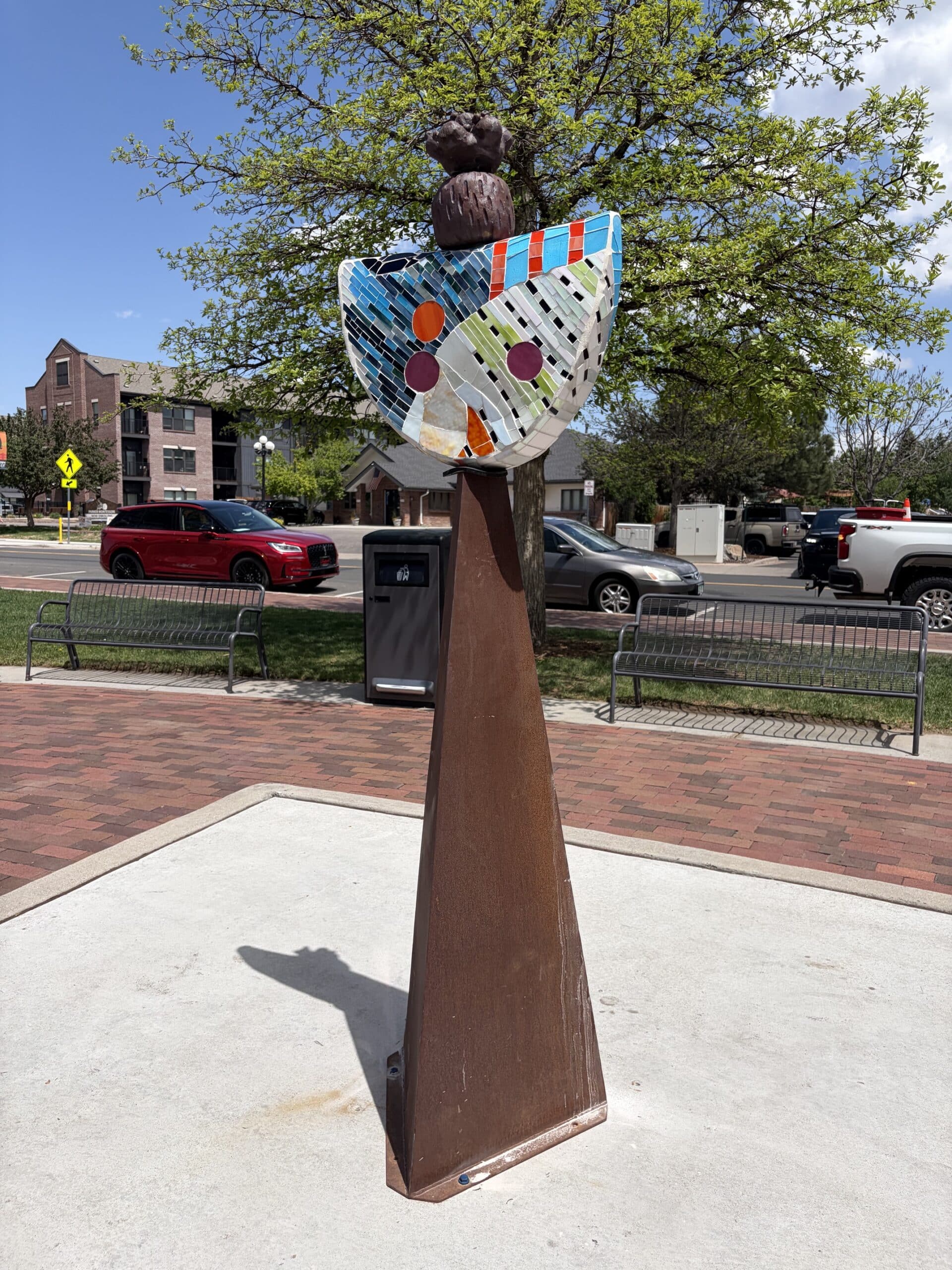 She Holds Up the Sky, Totem, is a sculpture consisting of stained glass mosaic and clay with a metal base.