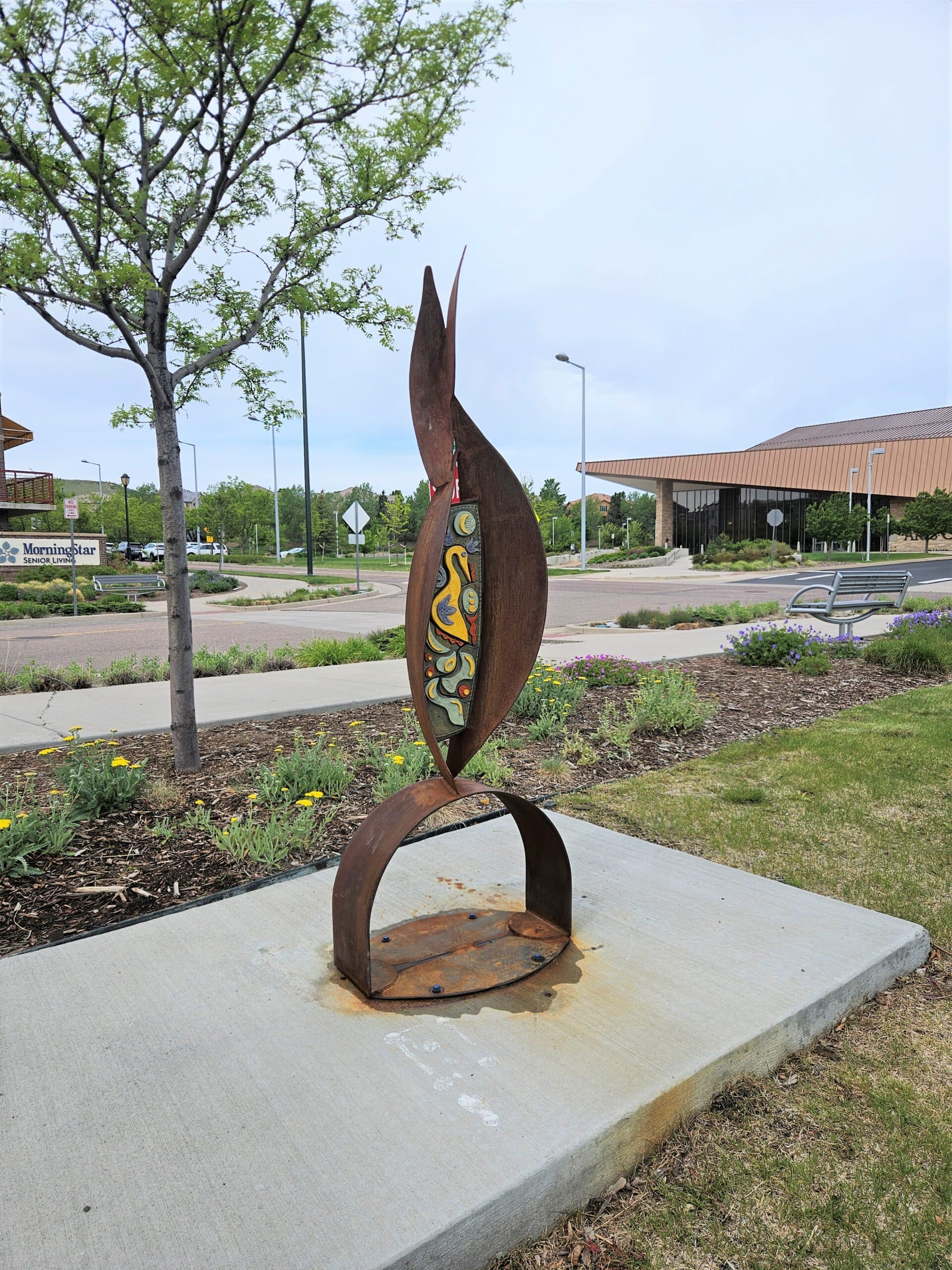 Source by artist Gregory Fields contains a curving of steel forms that cradle two ceramic relief panels.
