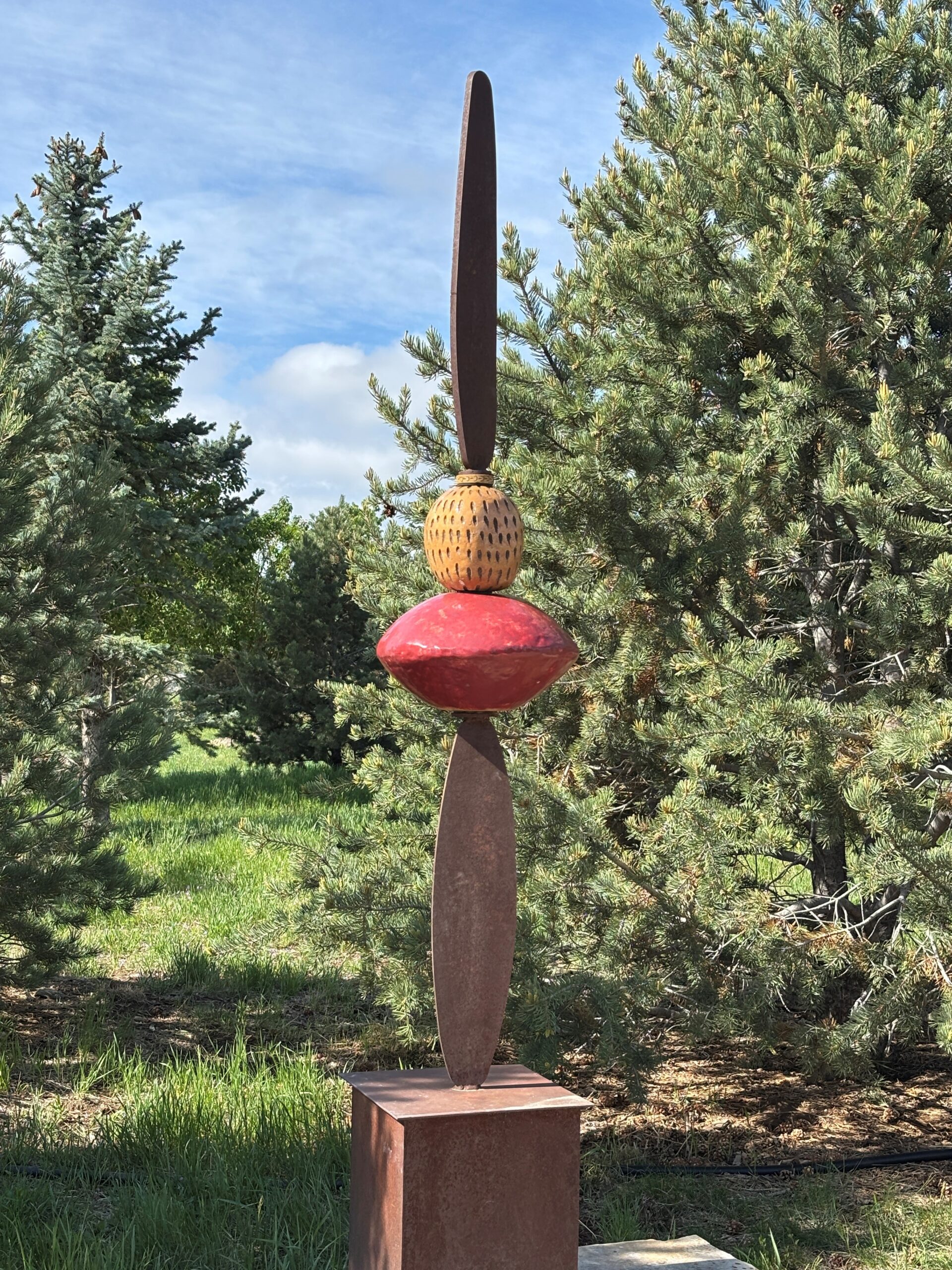 Transformation is a sculpture by Charlotte Zink with two oblong objects on both sides, along with a red diamond-shaped object and gold looking bead in the middle.