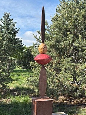 Transformation is a sculpture by Charlotte Zink with two oblong objects on both sides, along with a red diamond-shaped object and gold looking bead in the middle.