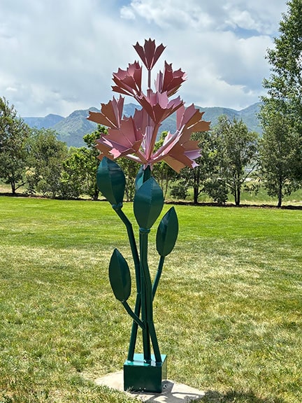 Wildflowers is a steel sculpture that is 10-feet tall with pink flowers and green leaves.